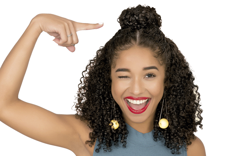 A modelo fez o penteado de Half Bun, ela apresenta uma expressão sorridente no rosto, sua mão direita aponta para o pequeno coque do seu penteado. 